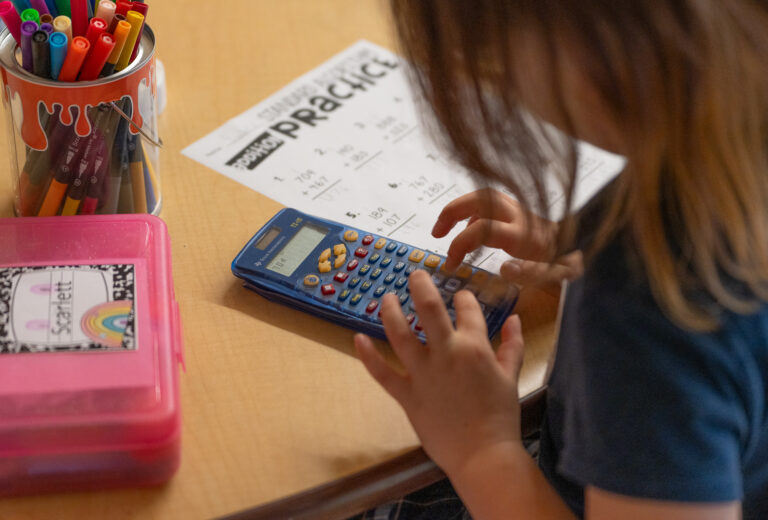 A young student practices her math equations while completing her homework with a calculator