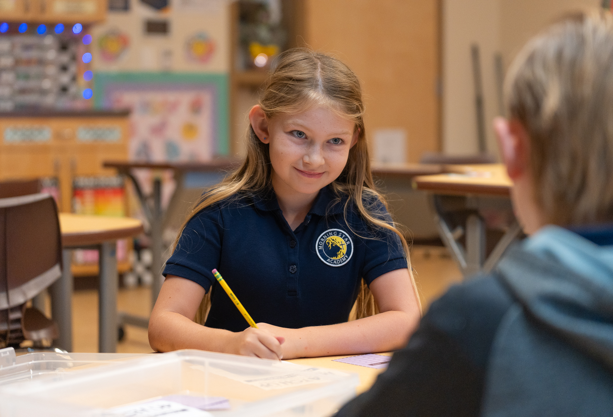 A young student smiles as she writes notes during class