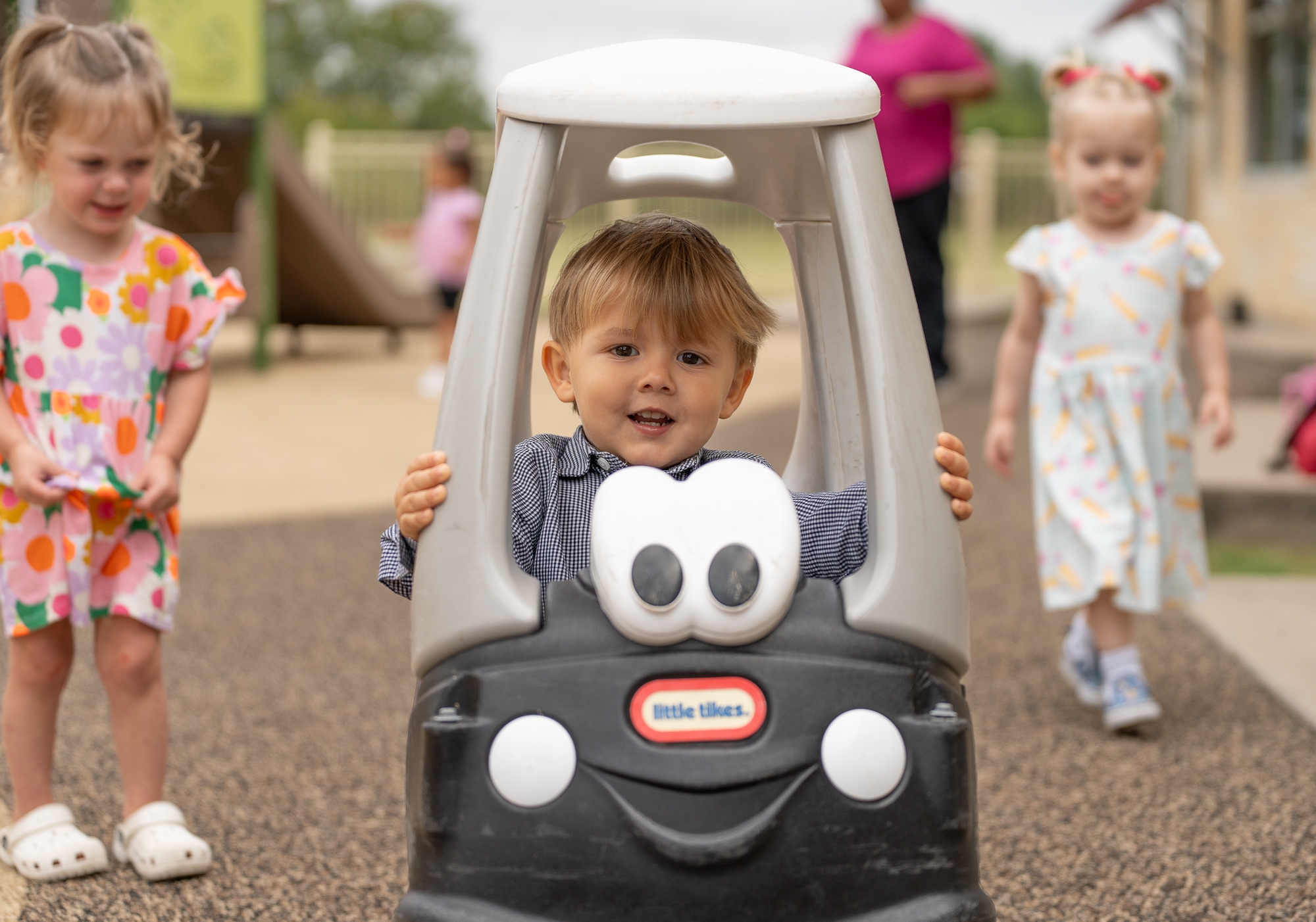 A young student smiles during recess while he sits in a little tikes cart outside