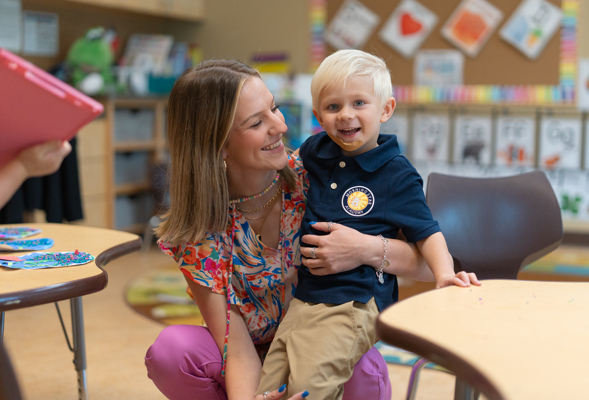 A young student smiles as his teacher picks him up during class