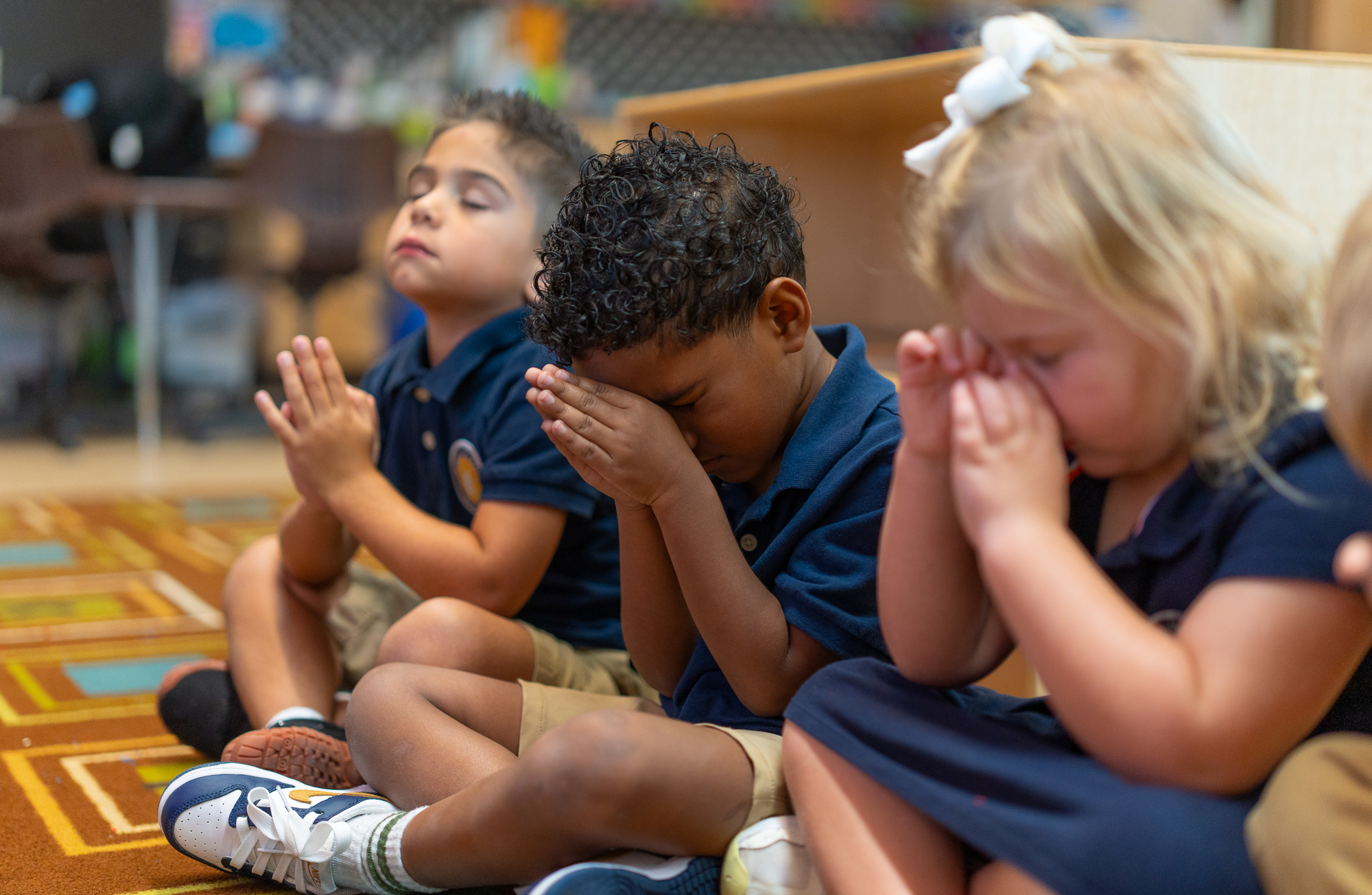 Three young students focus intently during prayer at school