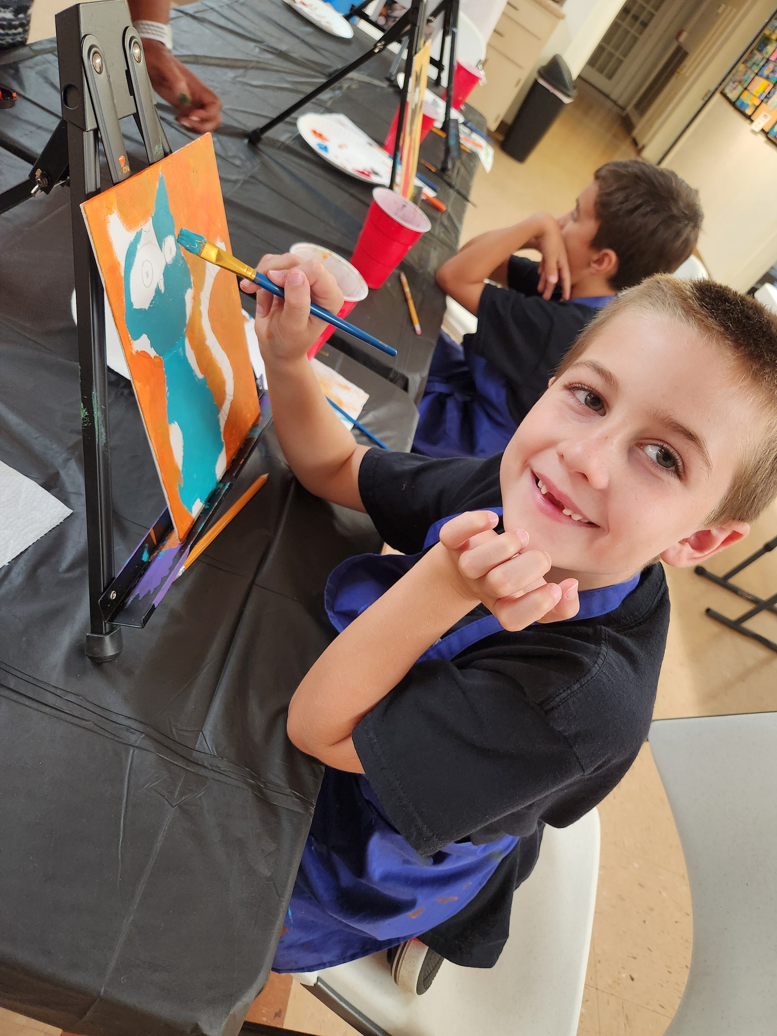 A student smiles as he paints a cat in art class